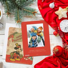 a christmas card with mickey mouse and other holiday decorations around it on a white wooden table