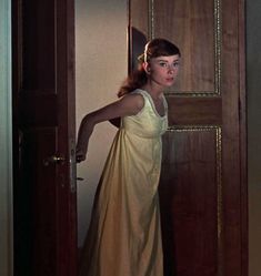 a woman standing in front of a door wearing a yellow dress and holding her arm out