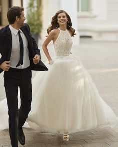 a bride and groom are walking down the street together in their wedding gowns, holding hands