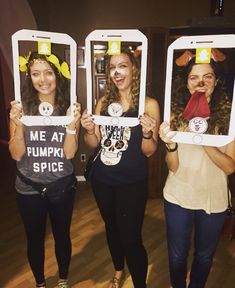 three women holding up cell phones with funny faces on them and one has a sign that says me at pumpkin spice