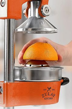 an orange is being squeezed into a juicer by a person's hand,