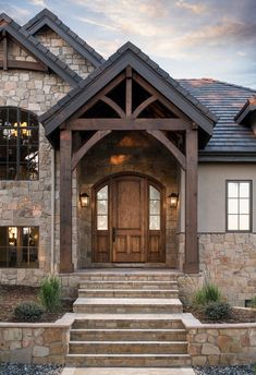 a stone and wood house with steps leading up to the front door that leads into the entrance