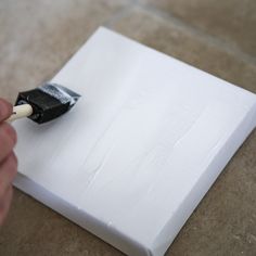 a person is using a brush to paint a square piece of paper