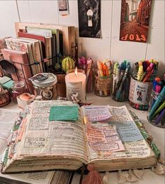 an open book sitting on top of a table covered in lots of books and writing utensils