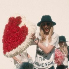 a woman holding up a giant heart made out of fake flowers with other people around her