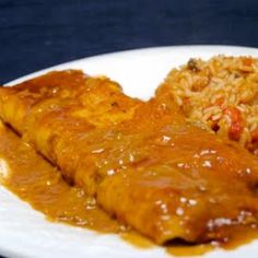 a white plate topped with meat covered in gravy next to rice and beans