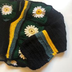 three crocheted sweaters with flowers on them sitting on a white table top