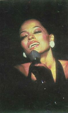 a woman singing into a microphone while wearing earrings