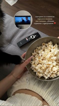 a woman is holding a bowl of popcorn and watching tv