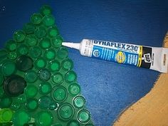 a tube of glue sitting on top of a piece of wood next to green plastic bottle caps