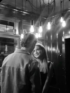 black and white photograph of man and woman in kitchen looking at each other with light bulbs overhead