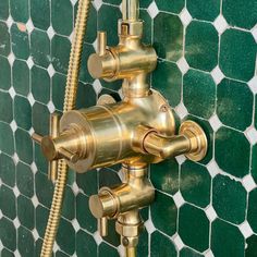 the faucet is attached to the green tiled wall with gold fixtures on it