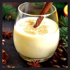 a glass filled with an eggnog drink surrounded by pine cones and cinnamon sticks