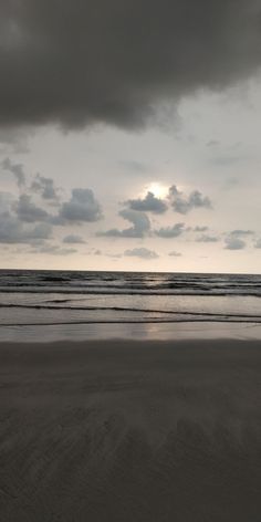 the sun is setting over the ocean with dark clouds in the sky, and some people are walking on the beach