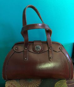 I am offering this graceful yet sturdy bag from the late 1950s/early 1960s. This dark brown leather bag has a nice hard satchel design with a nice mezzanine Luna curve. It has a double top handle and a pretty little keyhole latch. Please, be aware that their a little wear and mini mail scratches. Mid-century Brown Shoulder Bag For Travel, Antique Vintage Brown Formal Bag, Vintage Brown Antique Bag For Formal Occasions, Antique Brown Bags For Formal Occasions, Vintage Brown Formal Bag, Antique Style Vintage Brown Formal Bag, Retro Brown Formal Bags, Vintage Brown Formal Bags, Vintage Brown Satchel Bag