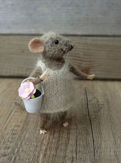 a stuffed mouse holding a flower in a white basket on a wooden table with wood planks