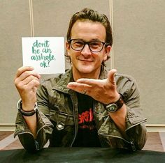 a man sitting at a table holding up a sign that says don't be an assorted ok