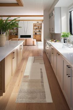 a long narrow kitchen with white cabinets and wood flooring, along with an area rug