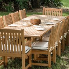 a wooden table with six chairs and plates on it in the middle of some grass