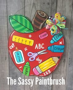 the sassy paintbrush apple is painted with school supplies on it and sits on a wooden surface