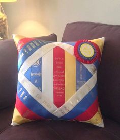 a decorative pillow on a brown couch with a lamp in the background and a blue, red, yellow and white ribbon around it