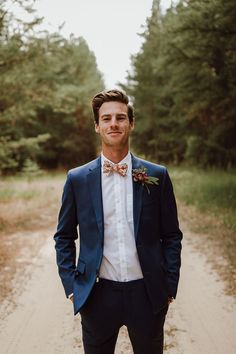 a man wearing a blue suit and bow tie standing in the middle of a dirt road