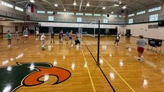 a group of people playing volleyball in an indoor gym with hard wood floors and large windows