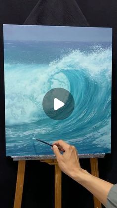 a person is painting an ocean wave on canvas