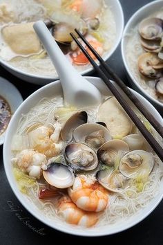 three bowls of soup with chopsticks in them and clams on the side