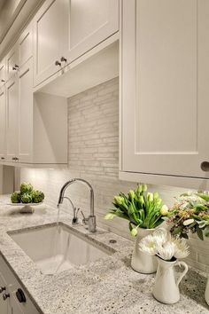 a kitchen with marble counter tops and white cabinets, along with green plants in vases