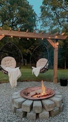 an outdoor fire pit with hanging chairs and lights on the top, surrounded by gravel