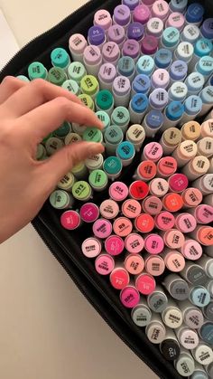 a person's hand is pointing at the letters on a large black case filled with colored crayons