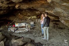 a man and woman standing next to each other in front of a cave with the word love written on it