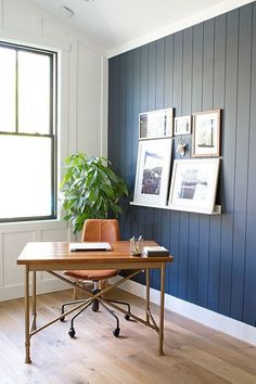 a wooden desk sitting in front of a window with pictures on the wall behind it