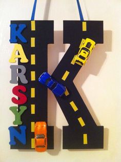 the letter k is made out of cardboard and has cars hanging from it's sides