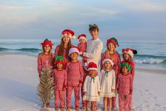 a group of people in christmas outfits sitting on the beach next to a small tree