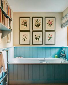 a bathroom with blue walls and pictures on the wall above the bathtub, along with bookshelves