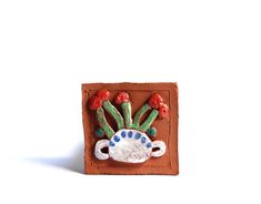 a ceramic tile with red flowers and green leaves on it's head, sitting in front of a white background