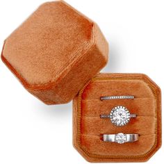 two engagement rings in an orange velvet ring box, one with a diamond center and the other with a white gold band