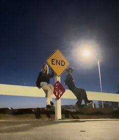 two people sitting on the end of a road under a street sign that says end