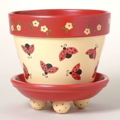 a red and white planter with ladybugs painted on the side, sitting in front of two smaller ones