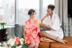 two women in robes sitting on a couch with champagne glasses and smiling at each other