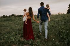 a man and woman holding hands as they walk through the grass with their two children