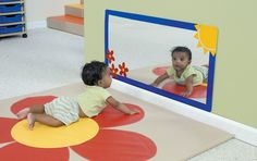 two toddlers playing in front of a mirror with their feet on the ground and looking at each other