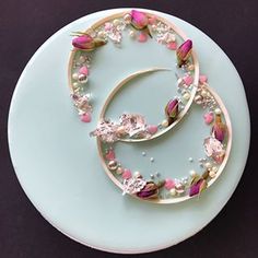 two pieces of jewelry sitting on top of a blue plate with pearls and pink flowers