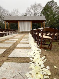 rows of chairs with white petals on the ground in front of an outdoor ceremony area