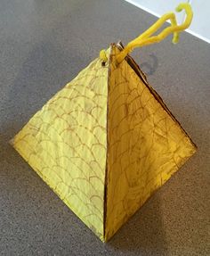 an origami piece with yellow string attached to it sitting on the floor in front of a white wall