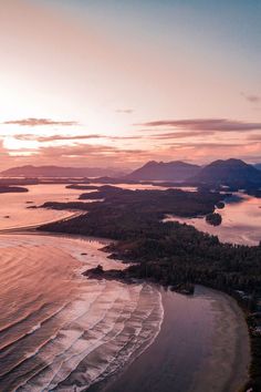 an aerial view of the beach and ocean at sunset with mountains in the back ground