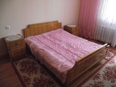 a bedroom with a bed, dresser and rug in the corner next to window curtained drapes