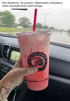 someone holding up a pink drink in their car